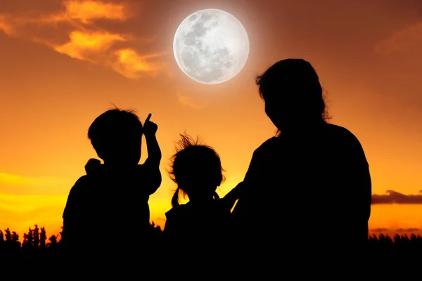 Силуэт счастливой семьи сидя и глядя на небо на закате . — стоковое фото