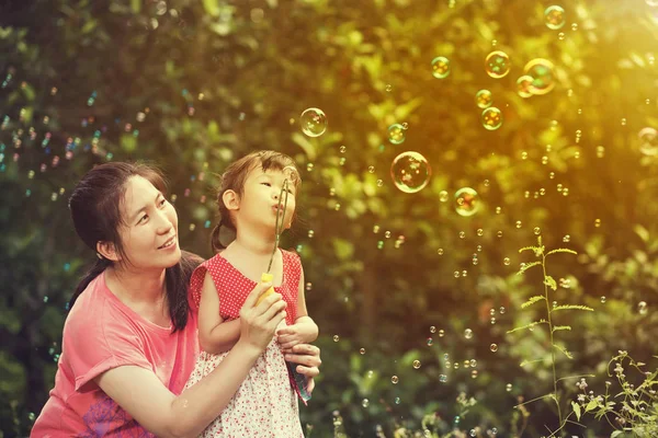 Asian lovely girl and her mother blowing soap bubbles. — Stock Photo, Image
