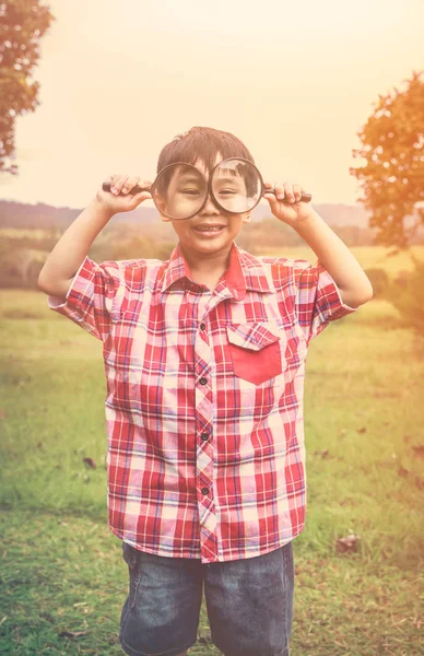 バカンス公園の虫眼鏡アジアの少年。暖かいトーン. — ストック写真