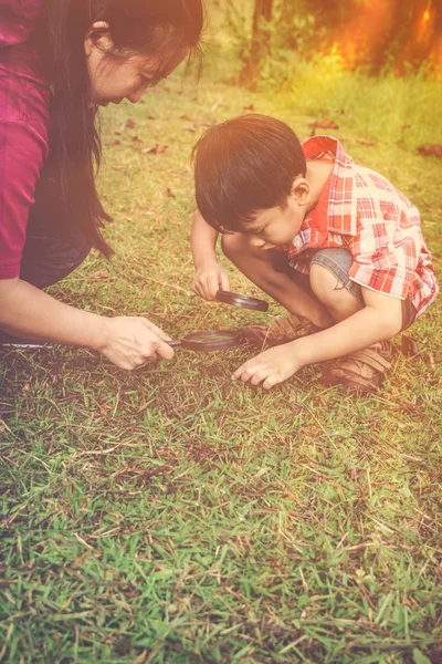 Madre e hijo asiáticos explorando la naturaleza con lupa . — Foto de Stock