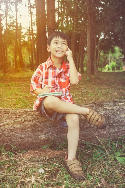 Gelukkig Aziatische kind lachend op houten log in nationaal park. Buitenshuis in de overdag. Onderwijs concept. — Stockfoto