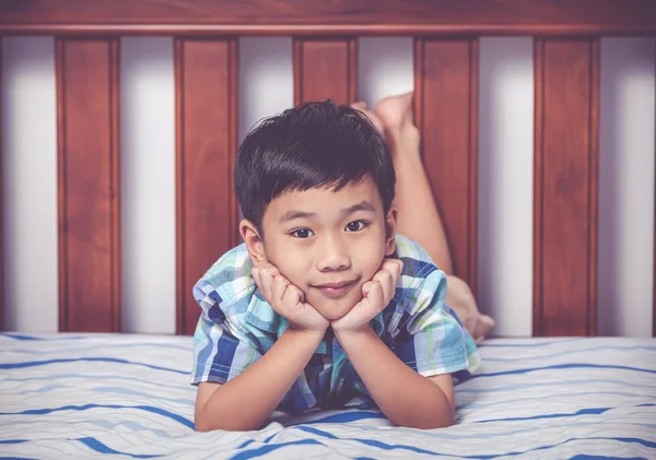 Rapaz bonito deitado descalço na cama no quarto. Criança feliz sorrindo . — Fotografia de Stock