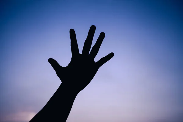 Silhouette of a hand on colorful sky background.