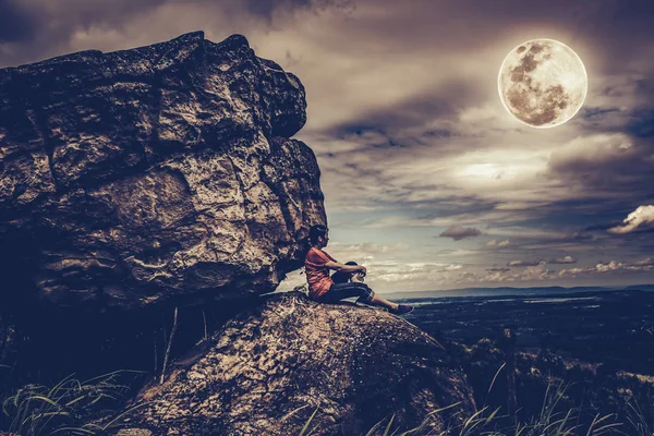 Mujer sentada sobre rocas, cielo nublado y luna llena. Estilo de llave baja . —  Fotos de Stock