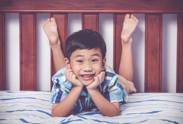 Handsome boy lying barefoot on bed in bedroom. Happy child smiling. — Stock Photo, Image