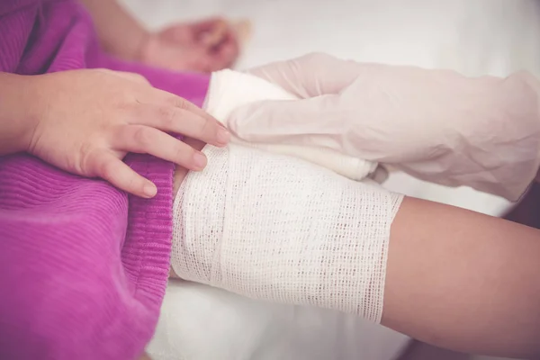 Bambino ferito. Medico pediatra che bendava il ginocchio del bambino. tono vintage . — Foto Stock