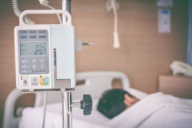 Asyalı çocuk hasta yatağının üzerinde infüzyon pompa intravenöz IV damlalıkla yalan
