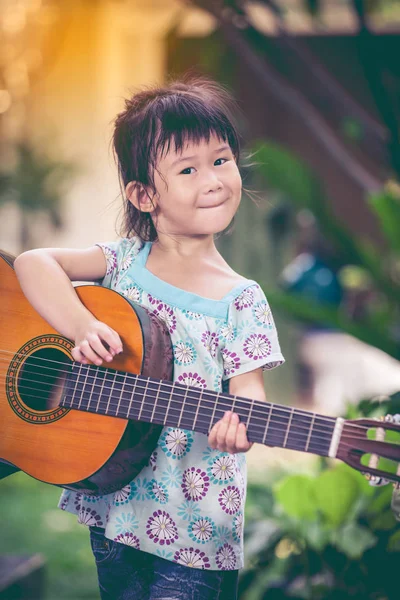 Asiatisches Kind beim Gitarrespielen. entzückendes Mädchen lächelt glücklich. — Stockfoto