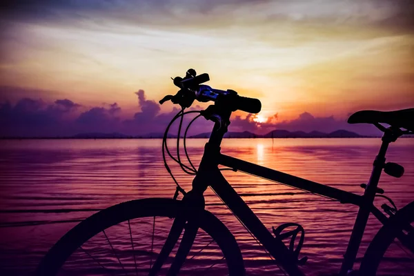 Silhouette di bicicletta sulla spiaggia contro il tramonto colorato nel mare . — Foto Stock