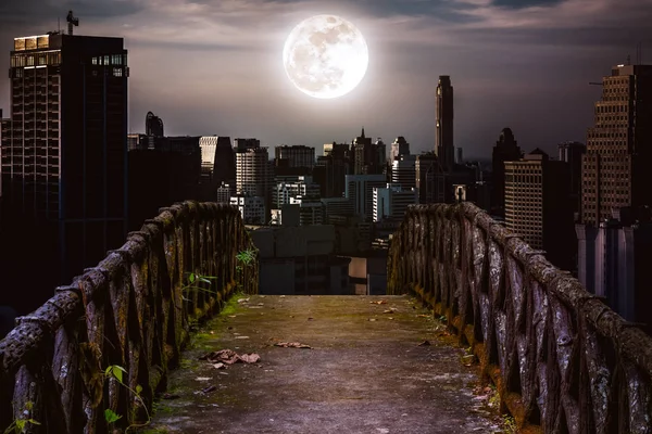 Viejo puente de hormigón a través de rascacielos con fondo super luna . — Foto de Stock