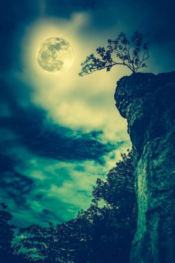 Gökyüzü bulutlu ve güzel dolunay ile karşı kayalar. İşlem çapraz.