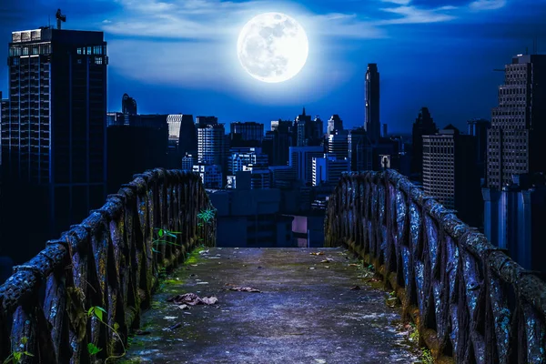 Viejo puente de hormigón a través de rascacielos con fondo super luna . — Foto de Stock