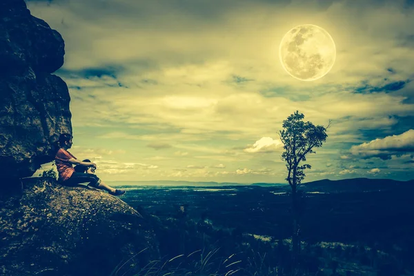 Жінка сидить на валунах, небо з похмурим і красивим повним місяцем . — стокове фото