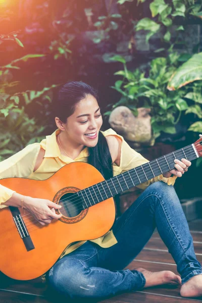 Asian kobieta gra gitara akustyczna z jasnym świetle słonecznym. Vintage efekt ton. — Zdjęcie stockowe