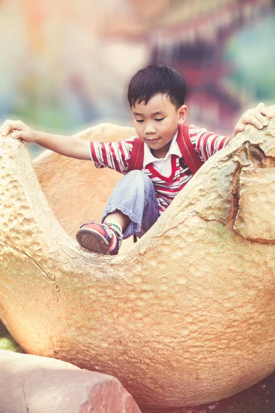 Niño asiático escalando huevos de dinosaurio de simulación. Concepto de juego al aire libre para niños —  Fotos de Stock