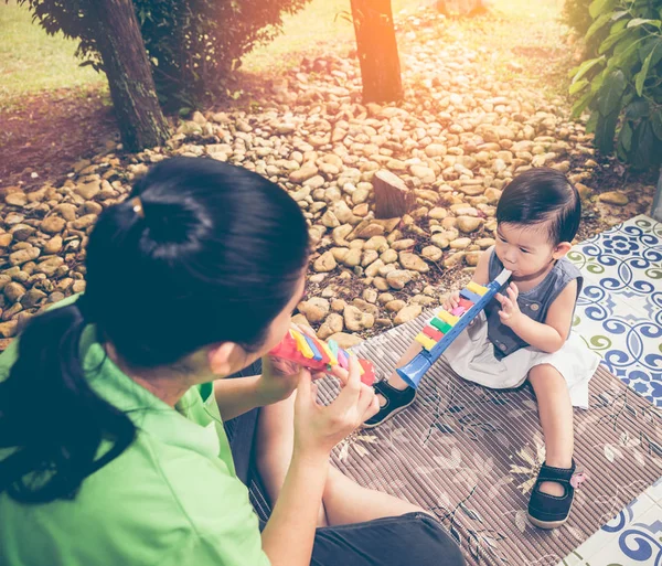 Asiatische Mutter spielt Kunststoff-Trompetenpfeife mit ihrer Tochter. — Stockfoto