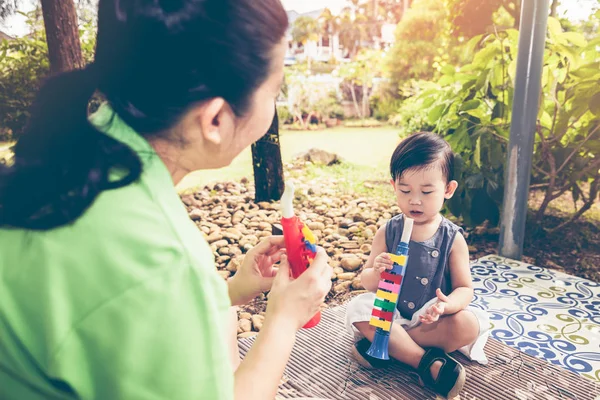 Mãe asiática tocando cachimbo de trompete de plástico com sua filha. Tom vintage . — Fotografia de Stock