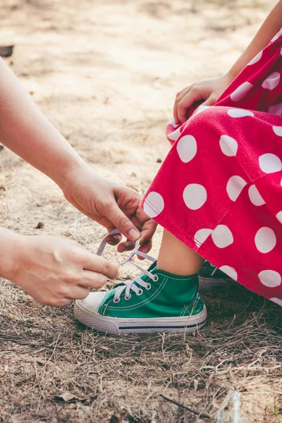 Una familia amigable. Madre cariñosa ayudando a su pequeña hija a atar cordones mientras pasan tiempo juntos — Foto de Stock