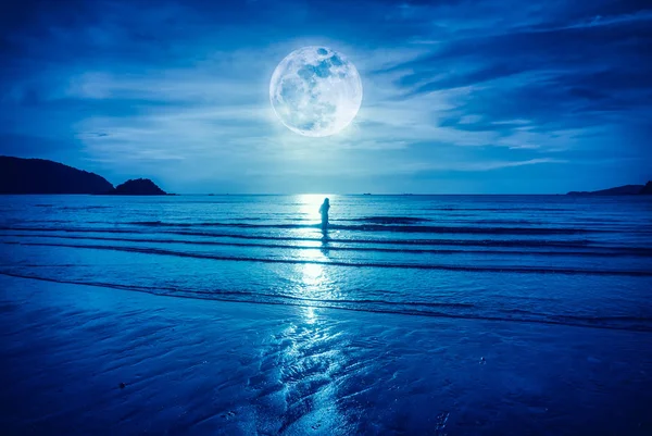 Super maan. Kleurrijke blauwe hemel met cloud en heldere full moon over zeegezicht en silhouet van de vrouw stond in de zee. — Stockfoto