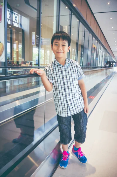 Happy asian child standing and smiling near electric speedwalk in modern airport. — Stock Photo, Image