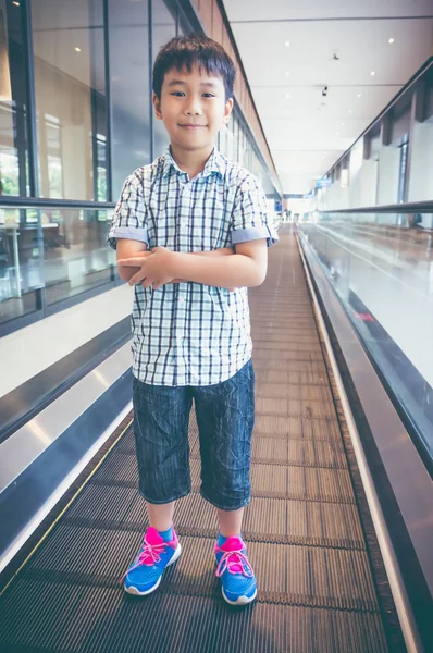 Happy asian child standing and smiling on electric speedwalk at modern airport. — Stock Photo, Image