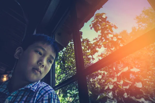 アジアの子の窓の近くに座っていると悲しい感じながらよそ見. — ストック写真
