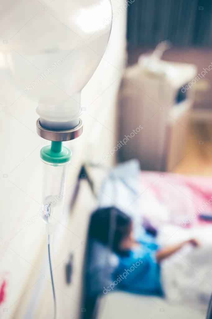 Illness asian girl sitting on sickbed in hospital with intravenous IV drip.
