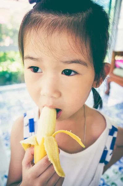 Nahaufnahme asiatisches Mädchen, das eine reife Banane schält und isst. Vintage-Ton. — Stockfoto