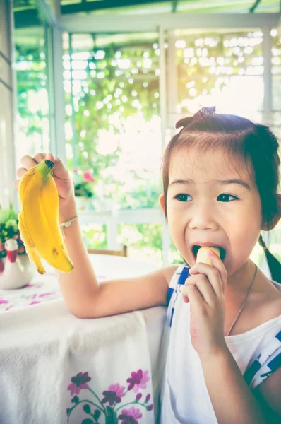 Adorabile ragazza asiatica mangiare una banana matura. tono vintage . — Foto Stock