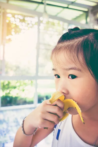 Asiatisches Mädchen schält und isst eine reife Banane. Vintage-Ton. — Stockfoto