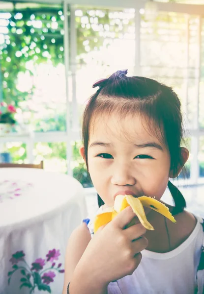 Entzückende asiatische Mädchen essen eine reife Banane. Vintage-Ton. — Stockfoto