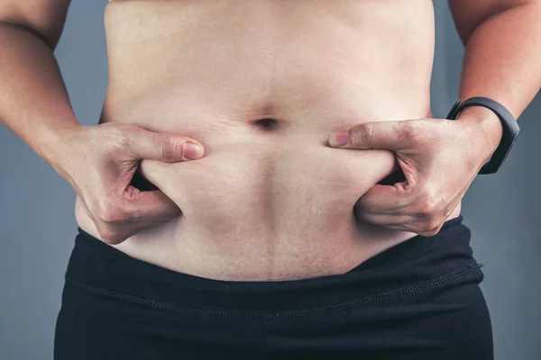 Close up female checking fat on abdomen, grey background. — Stock Photo, Image