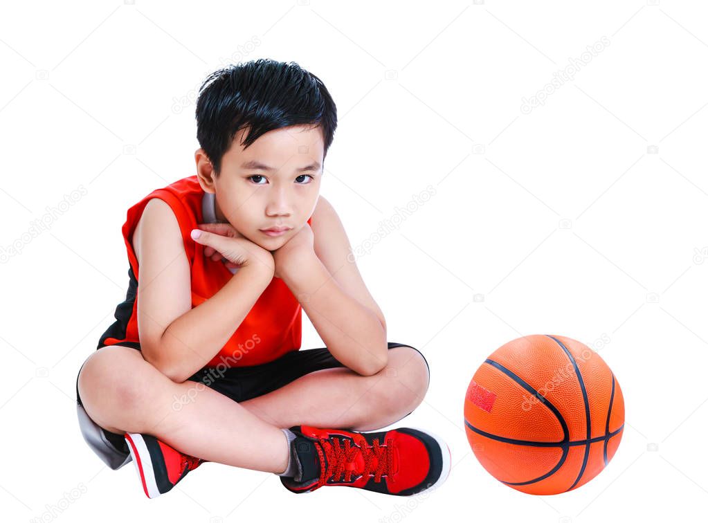 Unhappy asian child sitting near basketball. Isolated on white background.