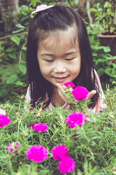Azjatycki dziecko podziwiając różowe kwiaty i przyroda wokół na podwórku. — Zdjęcie stockowe