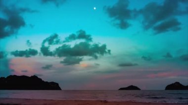 Gün batımından karanlığa 4k UHD 'lik hızlandırılmış görüntü. Mavi gökyüzü bulutlar deniz dalgaları üzerinde hareket ettikçe kararmaya başlar. Denizin üzerinde ay.