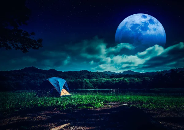 Great view of camping tent near lake at night with many stars. Beautiful full moon and cloudy with mountain range in the background. Serenity nature background. The concept of travel, tourism, camping
