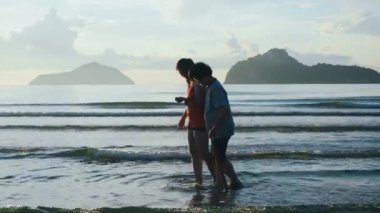 Anne ve kızı okyanus sahilinde yürümekten mutluluk duyarlar. Güneşin doğduğu sabah temiz havanın altında. Arka plan yumuşak okyanus dalgalarıdır..