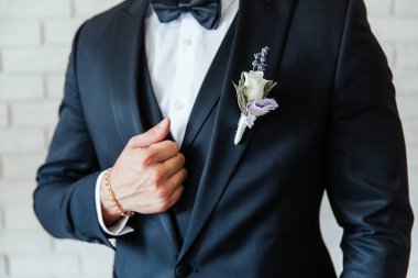 Siyah takım elbiseli damat, beyaz gömlekli bir smokin ve düğmeli bir delik.