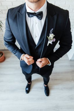 Siyah takım elbiseli damat, beyaz gömlekli bir smokin ve düğmeli bir delik.