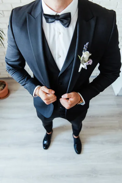 the groom in a black wedding suit, a tuxedo in a white shirt and a buttonhole