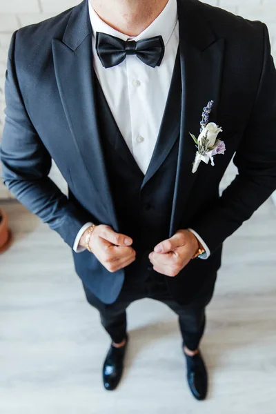 the groom in a black wedding suit, a tuxedo in a white shirt and a buttonhole