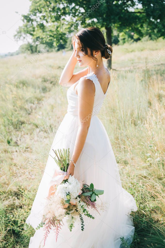 Bride in a luxurious white wedding dress in nature at sunset