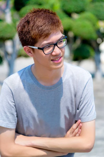 在泰国的公园里 一个头戴眼镜 面带笑容 面带微笑的年轻男子站在人们面前微笑 免版税图库图片