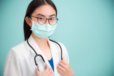 Stüdyo portresi, beyaz üniformalı güzel Asyalı kadın doktor, yeşil fotokopi arkaplanındaki kameraya bakarak Corona Virüsü 'nü sağlık açısından korumak için gözlük ve yeşil maske takıyor.