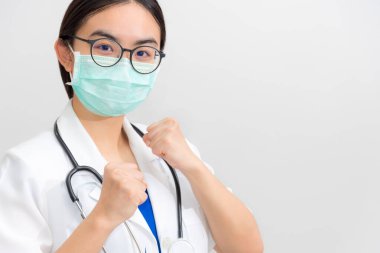 Beyaz üniformalı ve maskeli güzel Asyalı genç kadın doktor Coronavirus 'u koruyor, Doktor salgın hastalıklarla mücadelede hastaya destek olmak için yumruklarını kaldırıyor COVID 19, gri kopya alanı arka planı