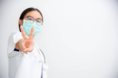 Stüdyo portresi güzel Asyalı genç kadın doktor iki V şeklinde parmak kaldırın. Salgın hastalıklarla mücadelede Coronavirus 'u desteklemek için maske takın. Boş gri arka planda 19 konsept.