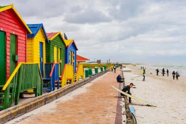 Cape Town, Güney Afrika, 28 Eylül 2013, sörfçü renkli plaj kulübe vintage soyunma odaları ile bir plajda otururken