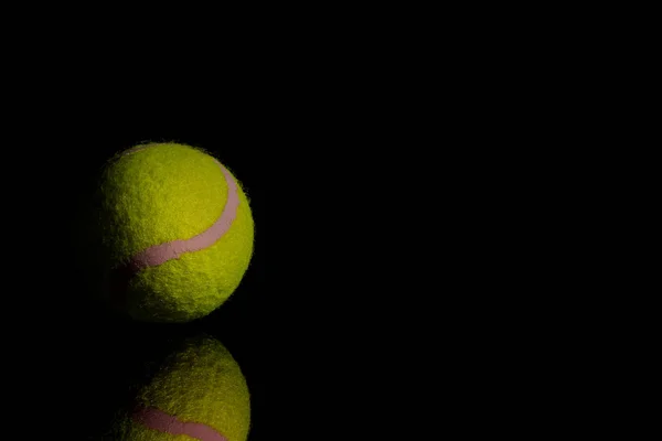 Koyu renkli aynada yansımalı parlak sarı tenis topu. — Stok fotoğraf