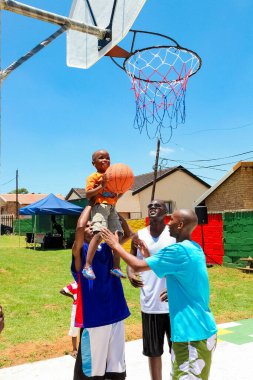 Soweto, Güney Afrika - 11 Aralık 2010: Afrikalı çocuk halka açık basketbol sahasında gol atmak için yetişkinlerden yardım alıyor