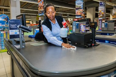 Cape Town, South Africa - March 23, 2020: Checkout cashier staff wiping down surfaces at Pick 'n Pay grocery store during virus outbreak clipart